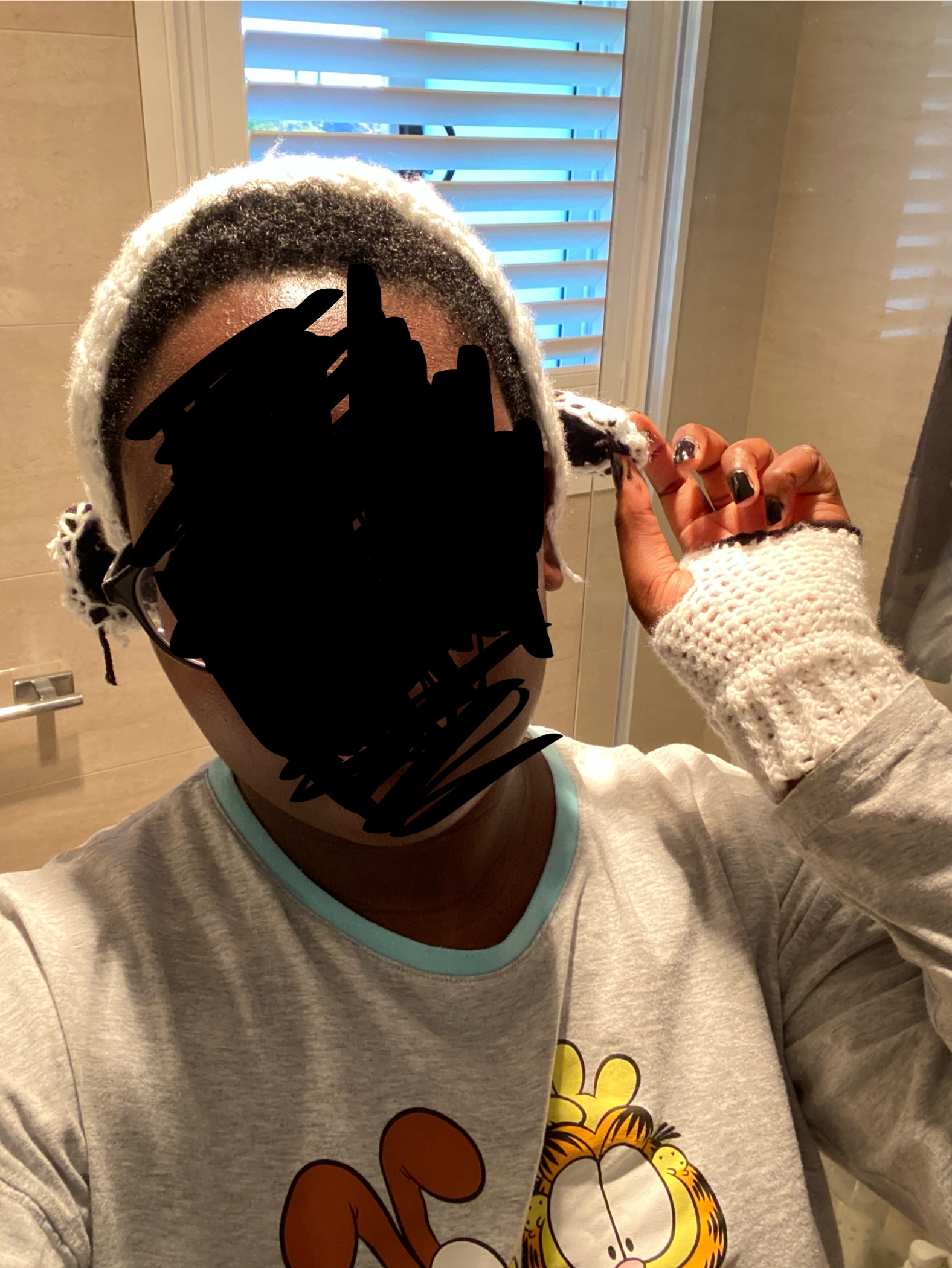 a dark skinned human presenting body with black nail polish, white crocheted earwarmers with sheep shaped ears and white fingerless gloves with a black trim.